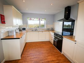 A kitchen with white cabinets wooden countertops a black stove and a window with a floral blind at Pen Y Cae in Llansannan