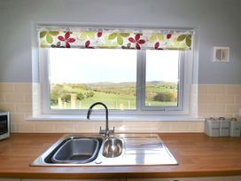 A kitchen sink and faucet below a window with a floral roller blind and countryside view at Pen Y Cae in Llansannan