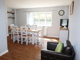 A dining room with a wooden table and white chairs next to a window and a black sofa with a green cushion at Pen Y Cae in Llansannan
