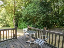A wooden deck with a small metal table and two metal chairs overlooking a garden with trees and grass at Badger View in Culverstone Green near Chatham