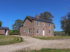 A two-story brick house with white framed windows and a gravel driveway surrounded by grass and trees at Foremans House in Bridlington