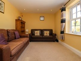 A living room with two brown sofas purple cushions bookcase table lamp window with curtains and flowers in vase at Foremans House in Bridlington