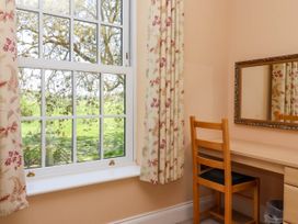 A wooden chair and desk with a mirror on the wall next to a window with floral curtains at Foremans House in Bridlington