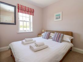 A bedroom with a double bed with striped pillows folded towels on bed a window with red and white striped blinds a bedside table with a lamp a mirror on wall and framed picture above bed at Foremans House in Bridlington