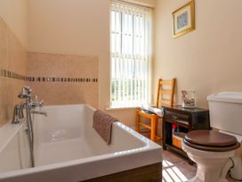 A bathroom with a bathtub a toilet a wooden chair a small dark wooden cabinet and a window with vertical blinds at Foremans House in Bridlington
