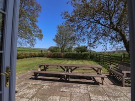 A patio with wooden picnic tables and a bench overlooking a garden with grass trees and a wooden fence at Foremans House in Bridlington