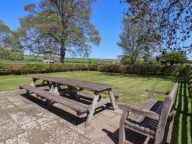 An outdoor patio with wooden picnic table and benches on grass surrounded by trees at Foremans House in Bridlington