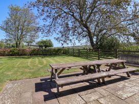 An outdoor patio area with wooden picnic tables and benches surrounded by grass and trees at Foremans House in Bridlington