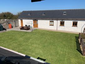 A courtyard with a green lawn a wooden picnic table and a white building with wooden doors and windows at The Mill and Stable in Laugharne