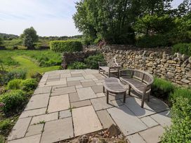 An outdoor seating area with stone patio and wooden furniture at Pheasant Cottage Beckside near Cartmel