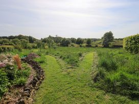 A garden with a winding path and trees at Pheasant Cottage Beckside near Cartmel