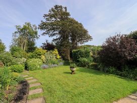 A garden with grass, flower beds, trees, and stepping stones at Kestrel Cottage near Cartmel