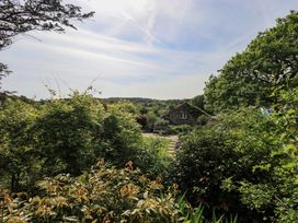 A garden with trees and a stone building in the background at Kestrel Cottage Beckside near Cartmel