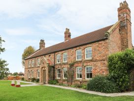 A brick house with multiple windows and chimneys with a grass lawn and outdoor furniture at Copmanthorpe Hall in Copmanthorpe