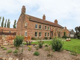 A brick house with multiple chimneys surrounded by a garden with plants and wooden chairs at Copmanthorpe Hall in Copmanthorpe
