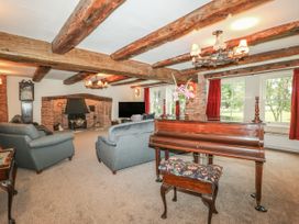 A living room with exposed wooden beams a grand piano gray sofas a brick fireplace and red curtains at Copmanthorpe Hall in Copmanthorpe