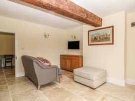 A living room with a sofa a wooden cabinet a wall-mounted television and a large ottoman at Copmanthorpe Hall in Copmanthorpe