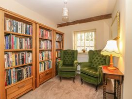A room with wooden bookshelves filled with books two green armchairs a window and a wooden side table with a lamp at Copmanthorpe Hall in Copmanthorpe