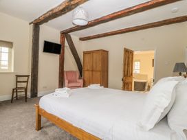 A bedroom with a double bed towels on bed wooden wardrobe pink armchair wall-mounted television and an open door leading to a bathroom at Copmanthorpe Hall in Copmanthorpe