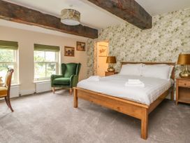 A bedroom with a wooden bed with white linens two bedside tables with lamps a green armchair two windows and floral wallpaper at Copmanthorpe Hall in Copmanthorpe