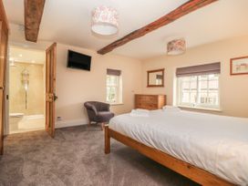 A bedroom with a bed a chair a chest of drawers a wall-mounted tv an ensuite bathroom and exposed ceiling beams at Copmanthorpe Hall in Copmanthorpe