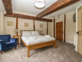 A bedroom with a wooden bed white bedding blue armchair bedside tables and exposed wooden ceiling beams at Copmanthorpe Hall in Copmanthorpe