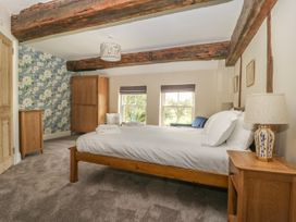 A bedroom with a wooden bed, bedside table with lamp, wardrobe, chest of drawers, two windows, exposed wooden beams, and floral wallpaper at Copmanthorpe Hall in Copmanthorpe
