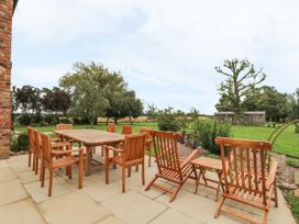 An outdoor patio area with wooden dining table and chairs set on a paved surface overlooking a grassy garden with trees and a shed at Copmanthorpe Hall in Copmanthorpe