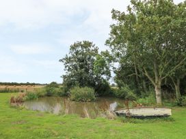 A small pond with bushes and trees surrounding it and a white boat on the grass near the pond at Copmanthorpe Hall in Copmanthorpe
