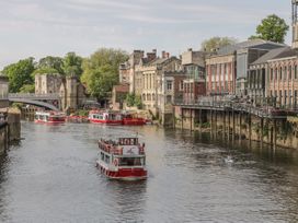 A river with tour boats and kayaks passing by historic buildings and a riverside walkway in York
