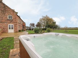 A hot tub on a patio next to a brick house with garden and trees at Copmanthorpe Hall in Copmanthorpe
