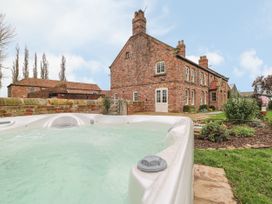 An outdoor hot tub in a garden with a brick house and a stone wall in the background at Copmanthorpe Hall in Copmanthorpe