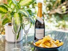A bottle of Nyetimber with champagne flutes and a bowl of potato chips in a garden setting at East Wing in Crewkerne