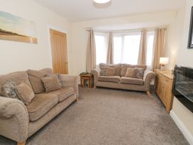 A living room with two beige sofas wooden door and cabinet with a lamp at Maesdu Cottage in Llandudno