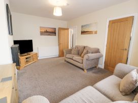 A living room with two sofas a television on a wooden stand and pictures on the walls at Maesdu Cottage in Llandudno