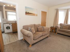A living room with two beige sofas and pillows next to a door leading to a kitchen with a washing machine at Maesdu Cottage in Llandudno