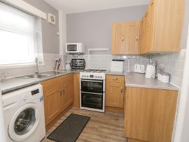 A kitchen with wooden cabinets a washing machine a gas stove a microwave and various kitchen appliances at Maesdu Cottage in Llandudno