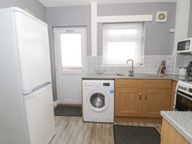 A kitchen with a refrigerator washing machine sink wooden cabinets and a door with a window at Maesdu Cottage in Llandudno