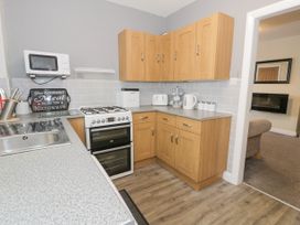 A kitchen with wooden cabinets a stove a microwave a toaster and a kettle at Maesdu Cottage in Llandudno