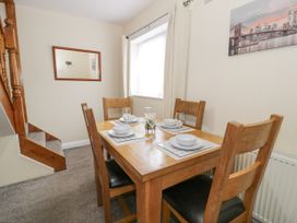 A dining area with a wooden table set for four beside a window and a staircase at Maesdu Cottage in Llandudno