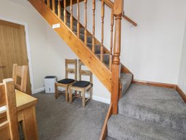 A stairway with wooden railing and carpeted steps next to two wooden chairs with cushions and a wooden table at Maesdu Cottage in Llandudno