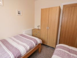 A bedroom with two single beds a wooden wardrobe a chest of drawers and a small framed picture on the wall at Maesdu Cottage in Llandudno