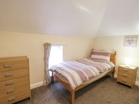 A bedroom with a single bed striped bedding a wooden dresser and bedside table with a lamp at Maesdu Cottage in Llandudno