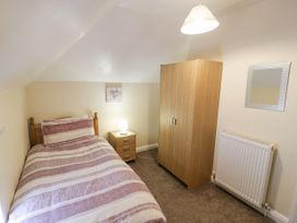 A bedroom with a single bed a bedside table with a lamp a wardrobe a radiator and a wall mirror at Maesdu Cottage in Llandudno