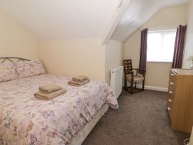 A bedroom with a bed with butterfly bedding towels on the bed a wooden chair a wooden dresser and a window with curtains at Maesdu Cottage in Llandudno