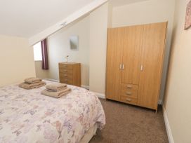 A bedroom with a bed with towels on it a wooden chest of drawers a wooden wardrobe a window with curtain and a mirror on the wall at Maesdu Cottage in Llandudno