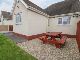 An outdoor area with a wooden picnic table on a gravel surface next to a cream colored house at Maesdu Cottage in Llandudno