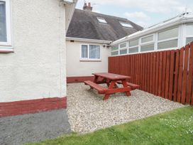 An outdoor area with a red wooden picnic table on gravel beside a building with white walls and a red fence at Maesdu Cottage in Llandudno