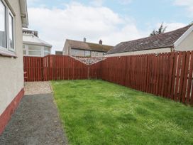 A backyard with grass and a red wooden fence surrounding it with a rotary clothesline in the center at Maesdu Cottage in Llandudno