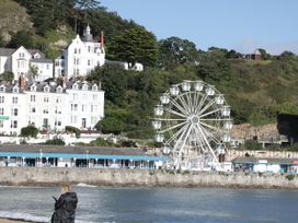 A ferris wheel near a waterfront with white buildings and green trees on a hill at Maesdu Cottage in Llandudno